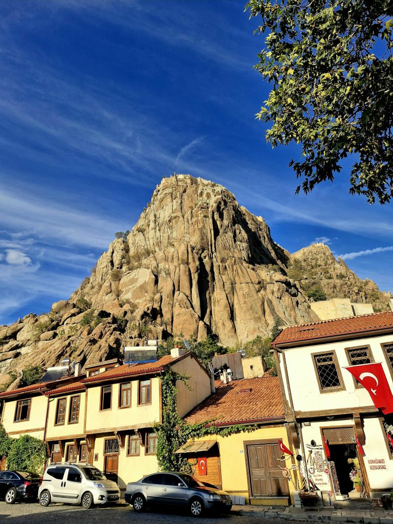Majestic rock formation with traditional Turkish buildings under clear blue skies.